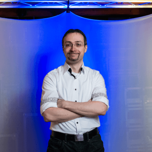 DJ Motzel steht lächelnd vor einem beleuchteten Traversentor.