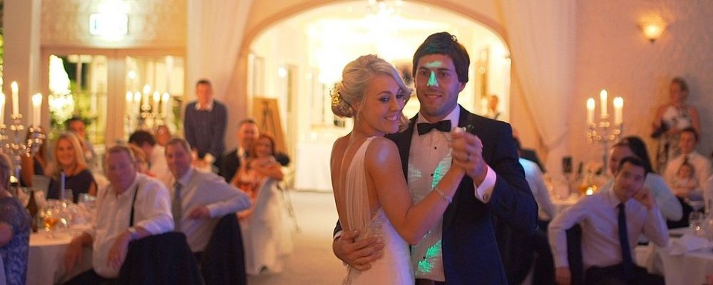 Paar beim tanzen zur Musik des Hochzeits DJ mit Gästen im Hintergrund